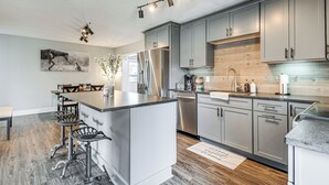 A modern kitchen with grey cabinets, a stainless steel refrigerator, and a bar area with stools.