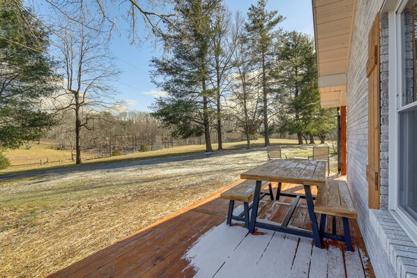 A wooden deck with a picnic table, a covered area, and a view of a wooded area.