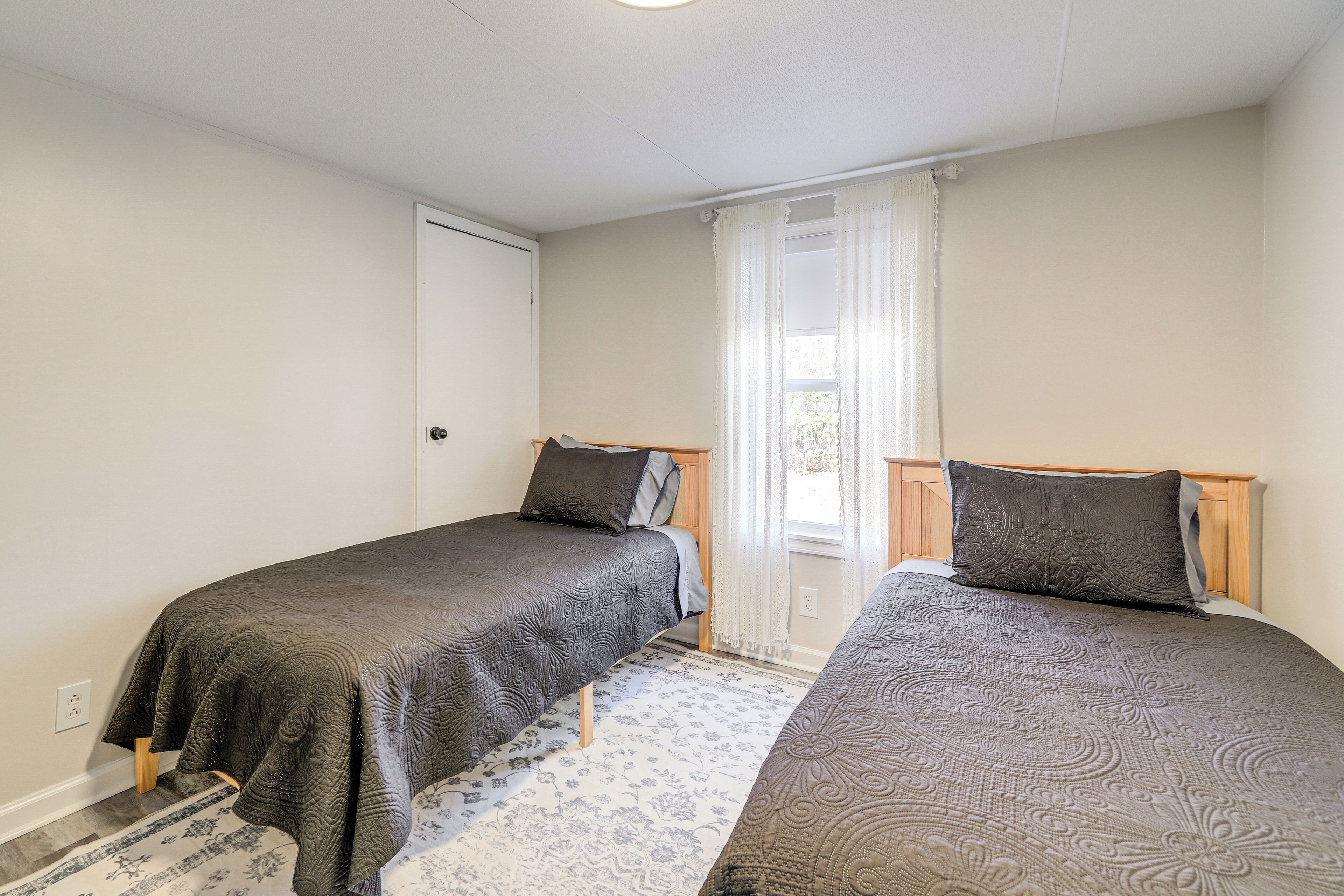 A bedroom with two single beds, a window with curtains, and a door.