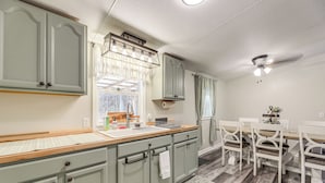 Una cocina con armarios verde claro, una encimera de madera y una zona de comedor con sillas blancas y una mesa.