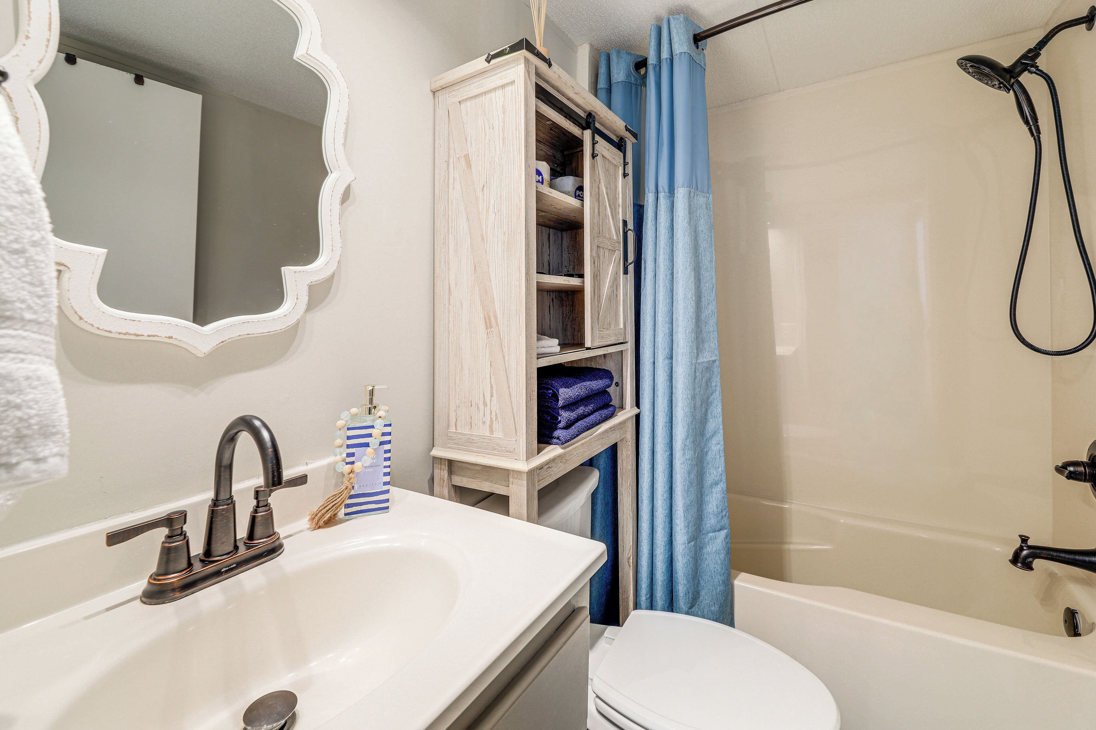 A bathroom with a white sink, a mirror, a wooden cabinet, a toilet, and a bathtub.