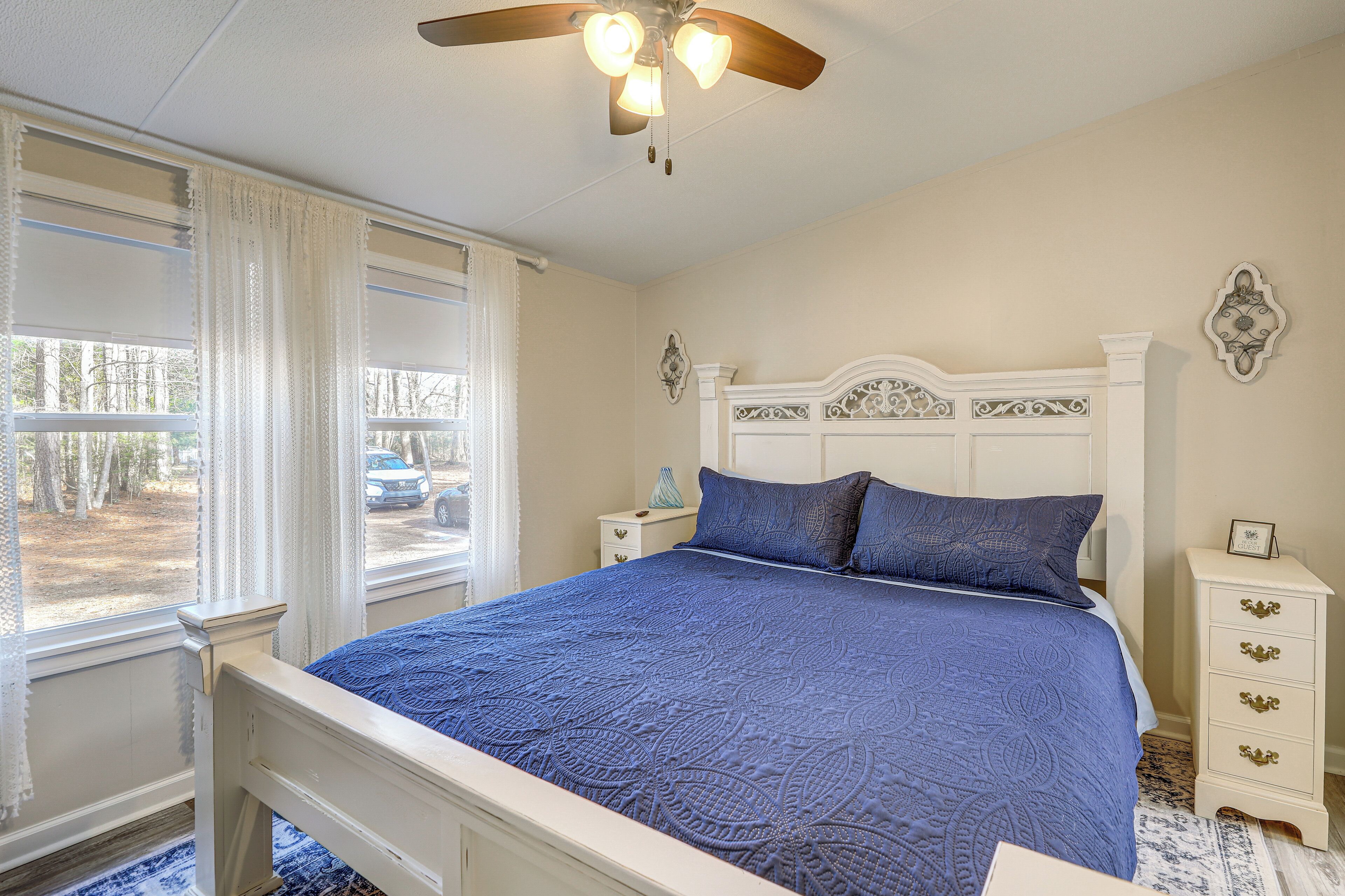 A bedroom with a bed, a nightstand, a dresser, a ceiling fan, and a window with curtains.