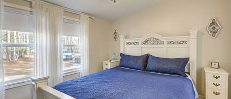 A bedroom with a bed, a nightstand, a dresser, a ceiling fan, and a window with curtains.