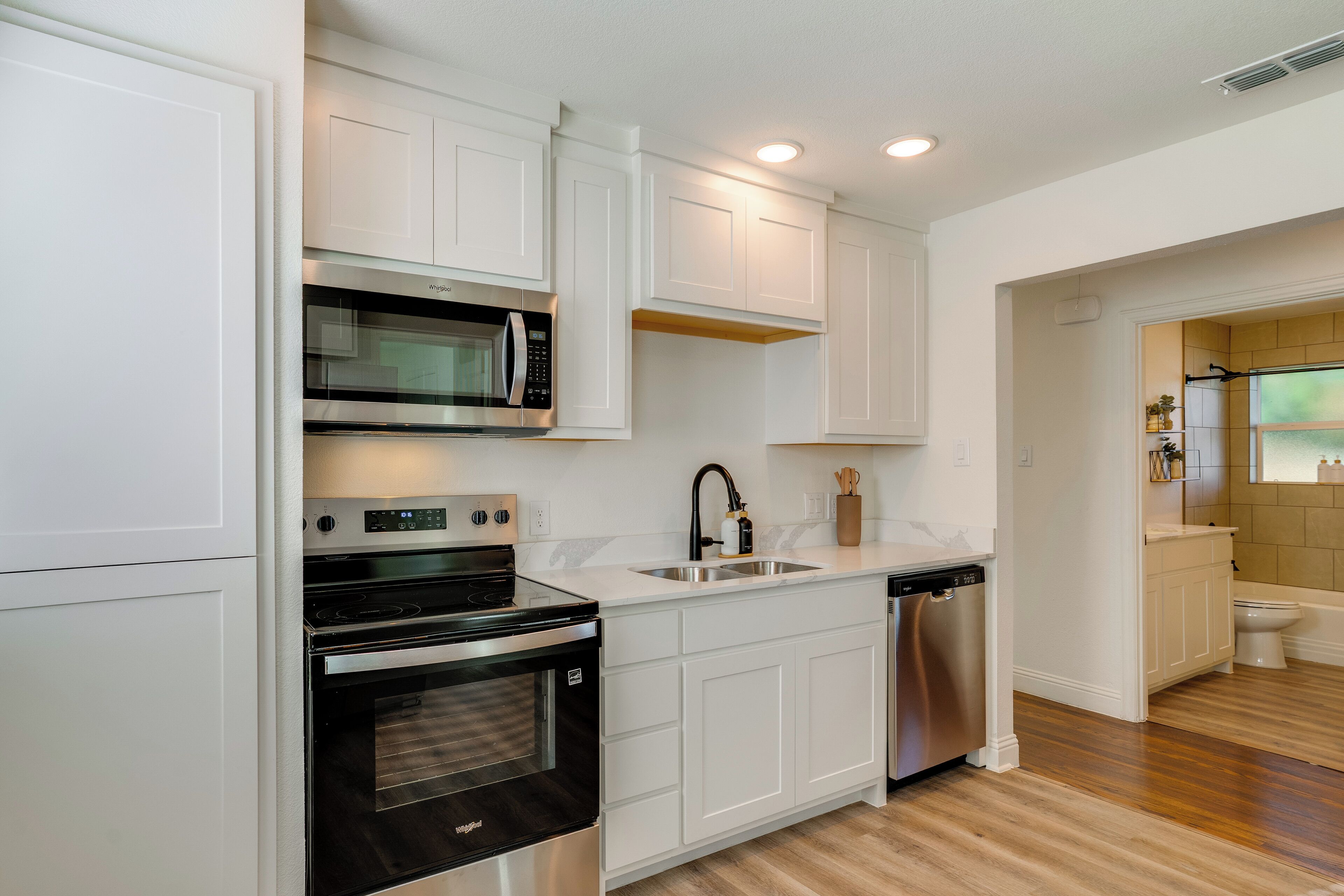 Una cocina moderna con armarios blancos, electrodomésticos de acero inoxidable y piso de madera.
