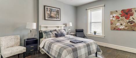 A bedroom with a bed, nightstands, a chair, a ceiling fan, a window, and artwork on the walls.