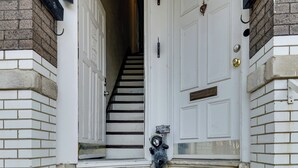 Une porte blanche avec une petite boîte aux lettres et une autre boîte aux lettres ornée d’une figurine d’ours, toutes deux placées devant le seuil de la porte.