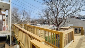 Une terrasse en bois avec des garde-corps, des fondations en béton et une vue sur un quartier résidentiel avec des maisons et des arbres.