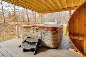 Un bain à remous avec un revêtement extérieur en pierre, une terrasse en bois et deux chaises.
