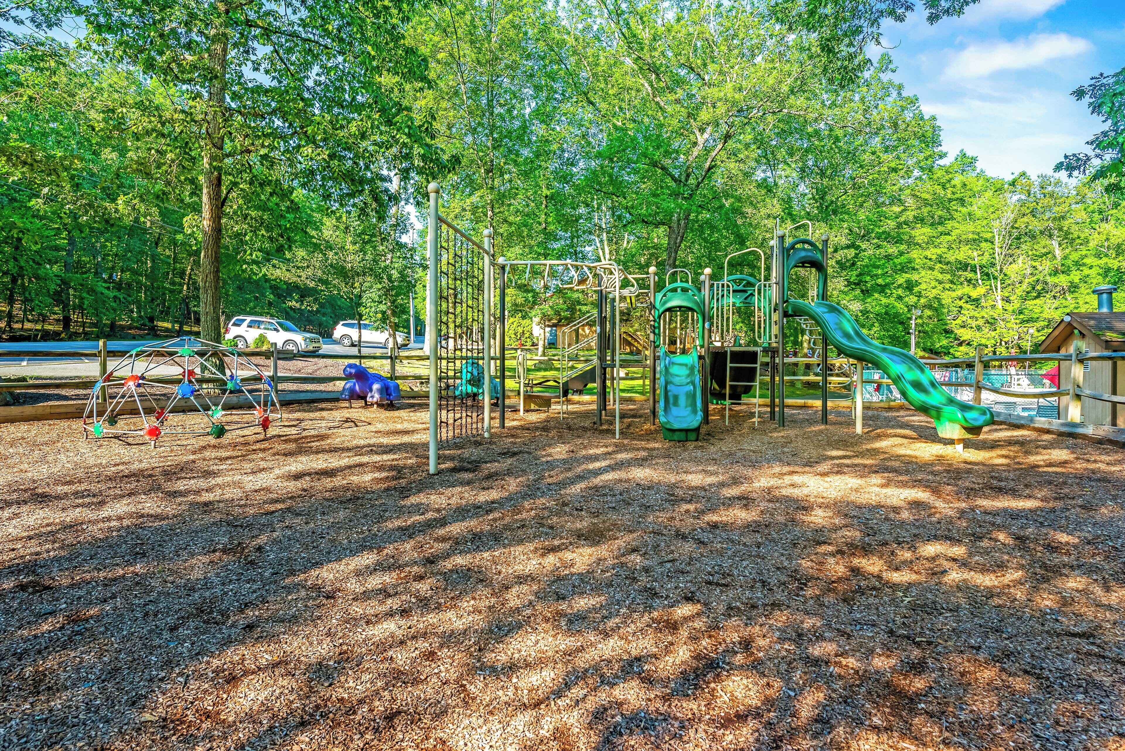 A playground with various play structures, including a slide and swings, surrounded by trees.