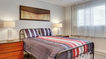 A neatly arranged bedroom with a metal bed frame, a wooden nightstand, two bedside lamps, and a large abstract painting on the wall.