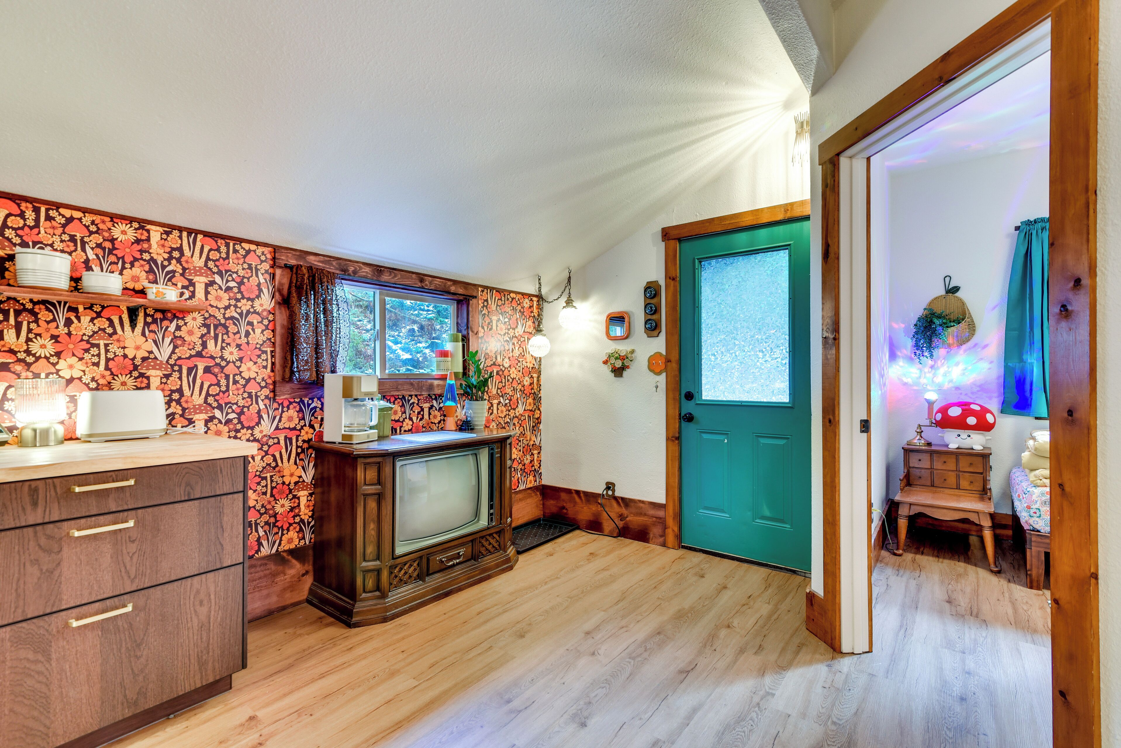 A cozy kitchen with wooden cabinets, a vintage television, and a teal door leading to another room.