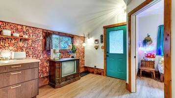 A cozy kitchen with wooden cabinets, a vintage television, and a teal door leading to another room.