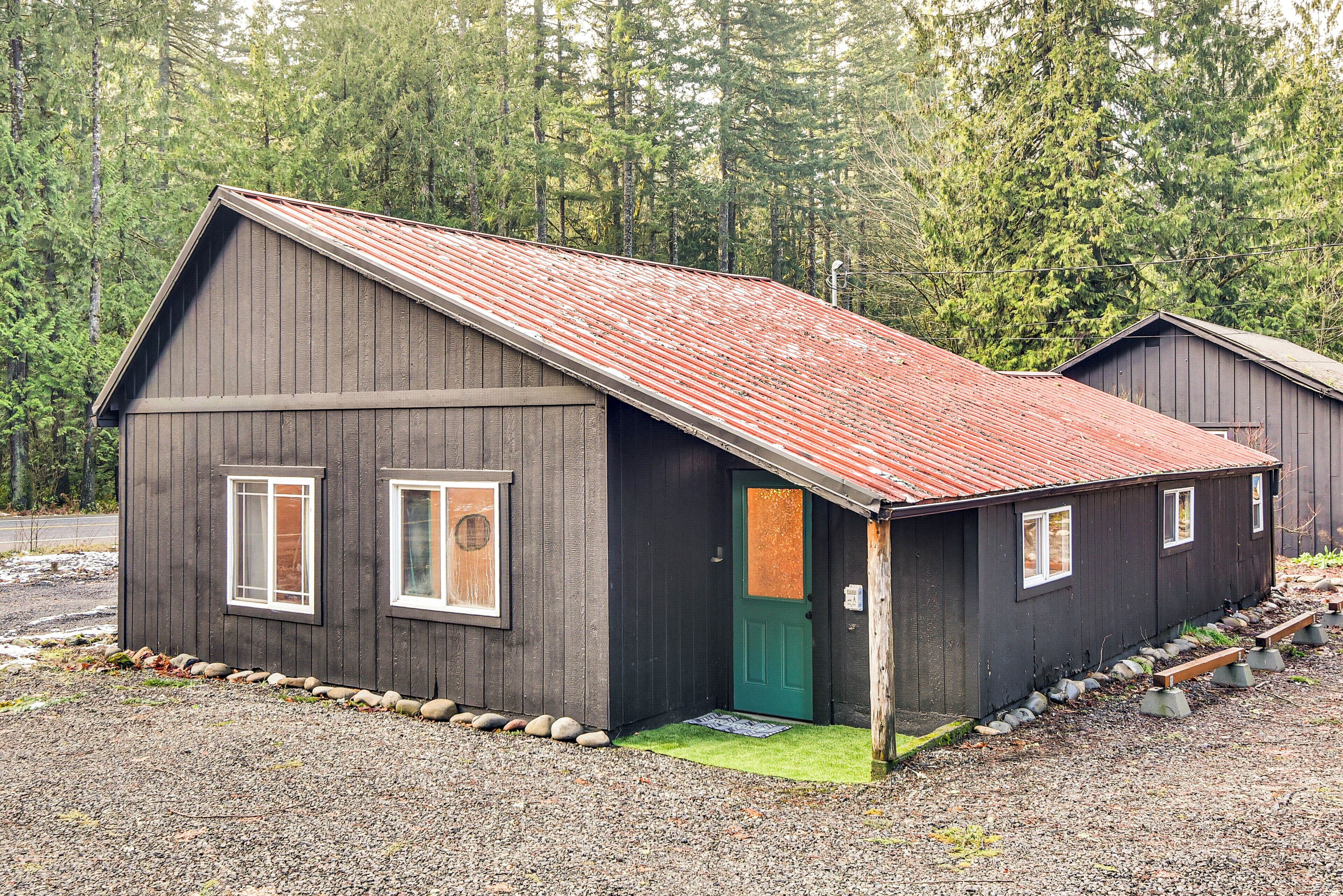 A rustic cabin with a sloped roof, a green door, and a gravel driveway.