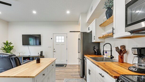 Una cocina moderna con armarios blancos, encimera de madera, refrigerador de acero inoxidable y horno empotrado.