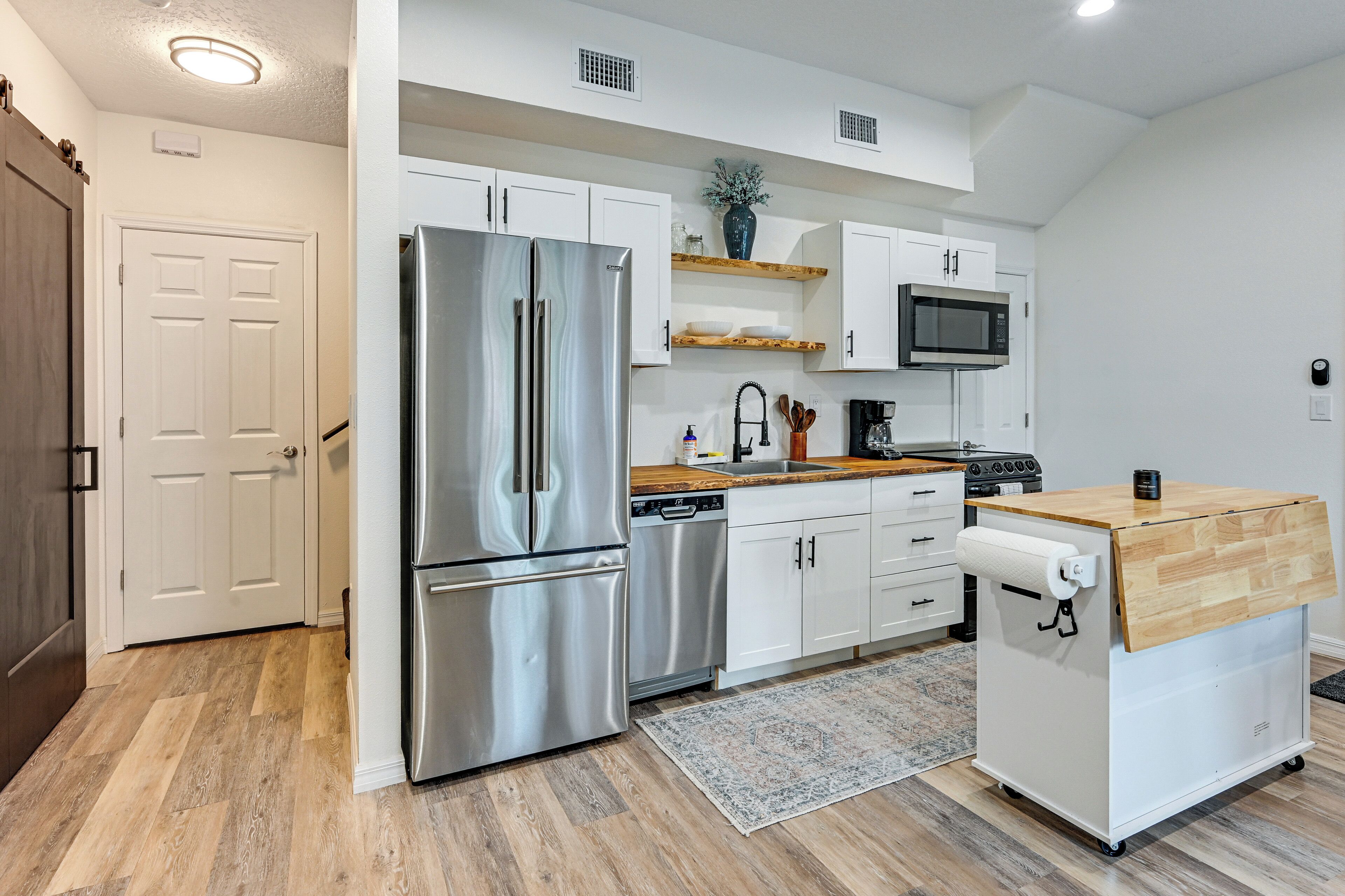 A modern kitchen with white cabinets, a stainless steel refrigerator, a microwave, and a coffee maker.