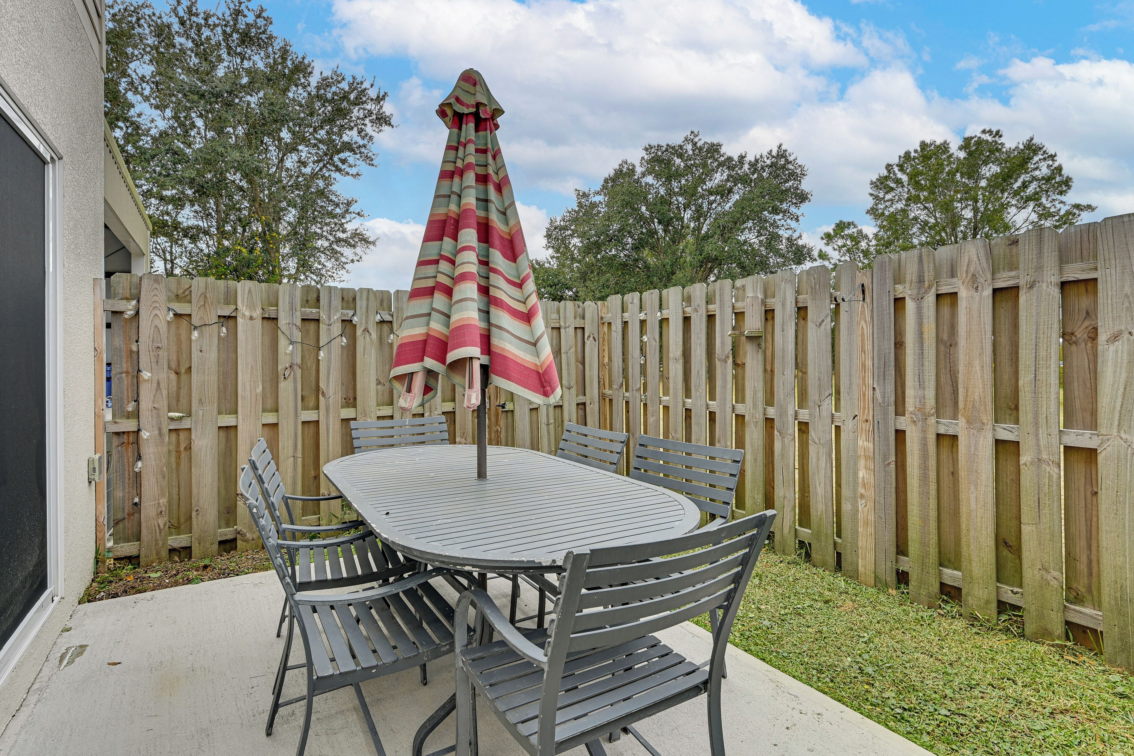A patio with a round metal table and six chairs, an umbrella, and a wooden fence in the background.