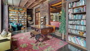 A cozy library with wooden bookshelves, a large wooden table, and a red carpeted floor. - Expansive Eagle Lake Escape w/ Boathouse + Beach (Ticonderoga)