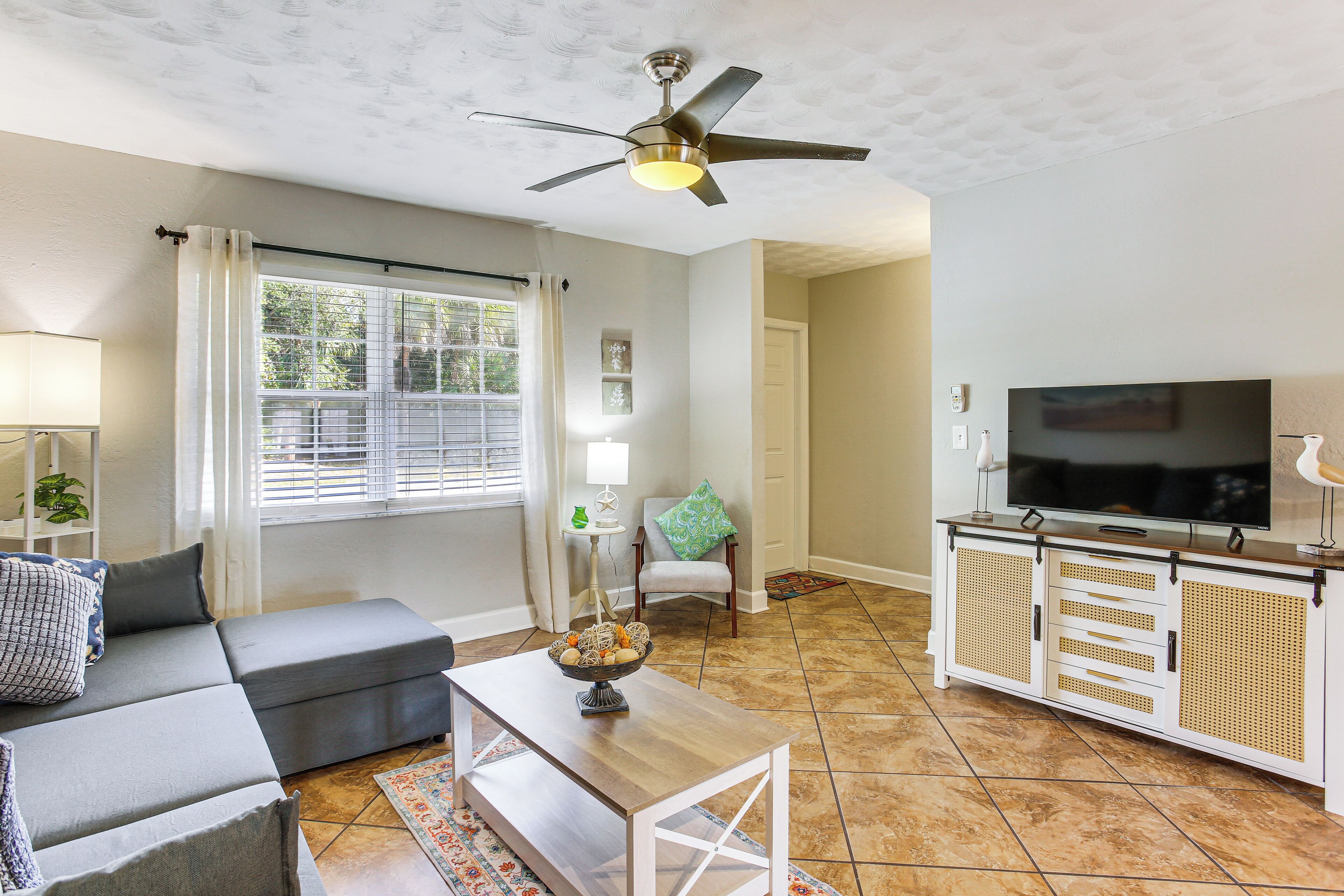 A living room with a grey sofa, a coffee table, a TV stand, and a ceiling fan.