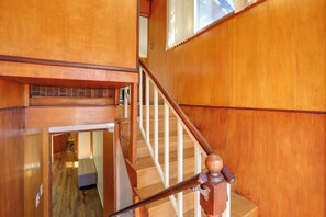 Eine Holztreppe mit Geländer und Blick auf einen Raum mit einer Bank und einer Tür am unteren Ende.