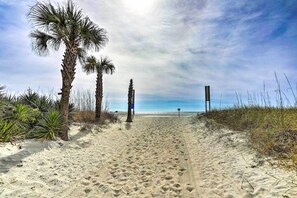 Een zandpad aan het strand, met palmbomen en een houten constructie in de verte.