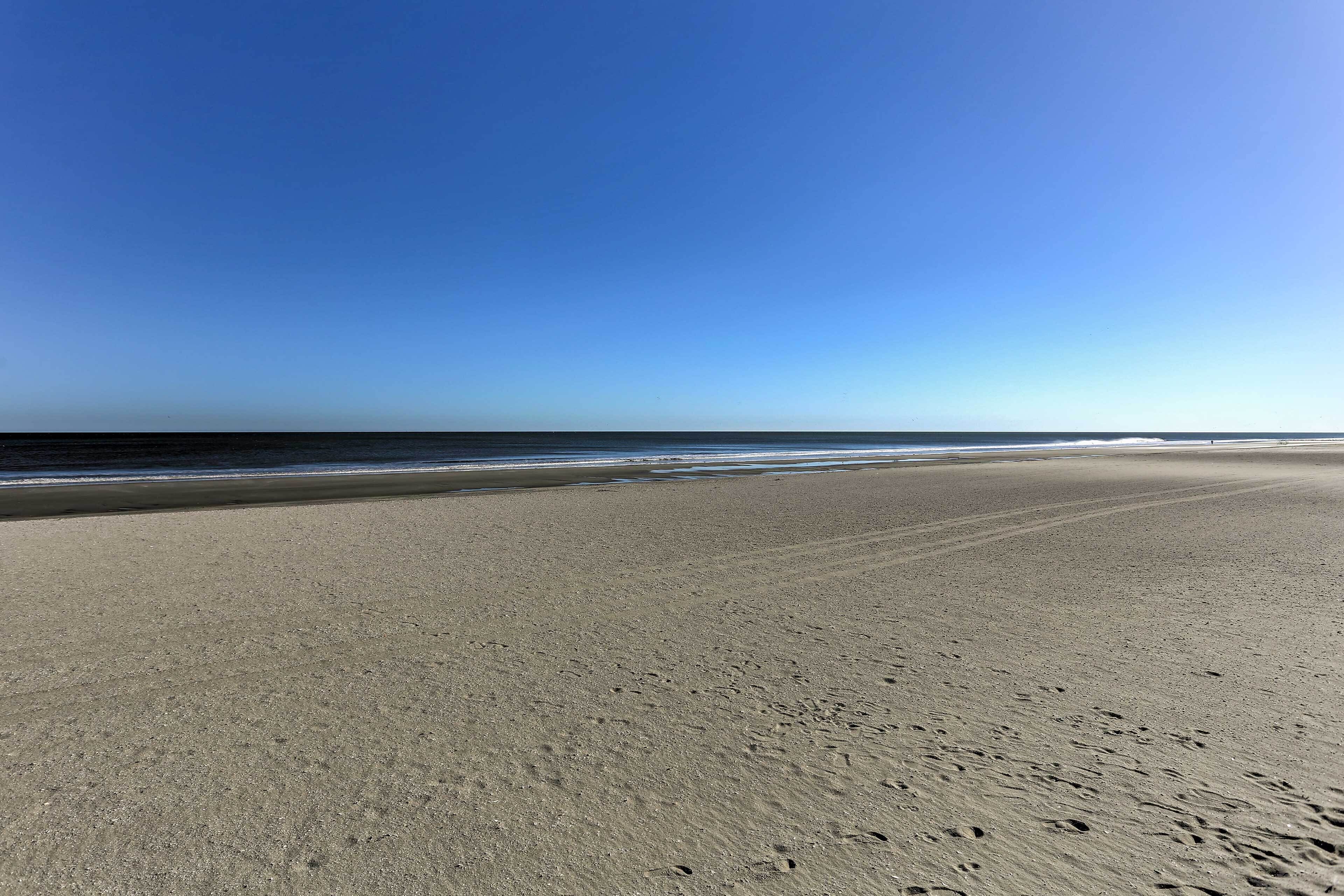 Una playa amplia y arenosa con huellas que van hacia el agua.