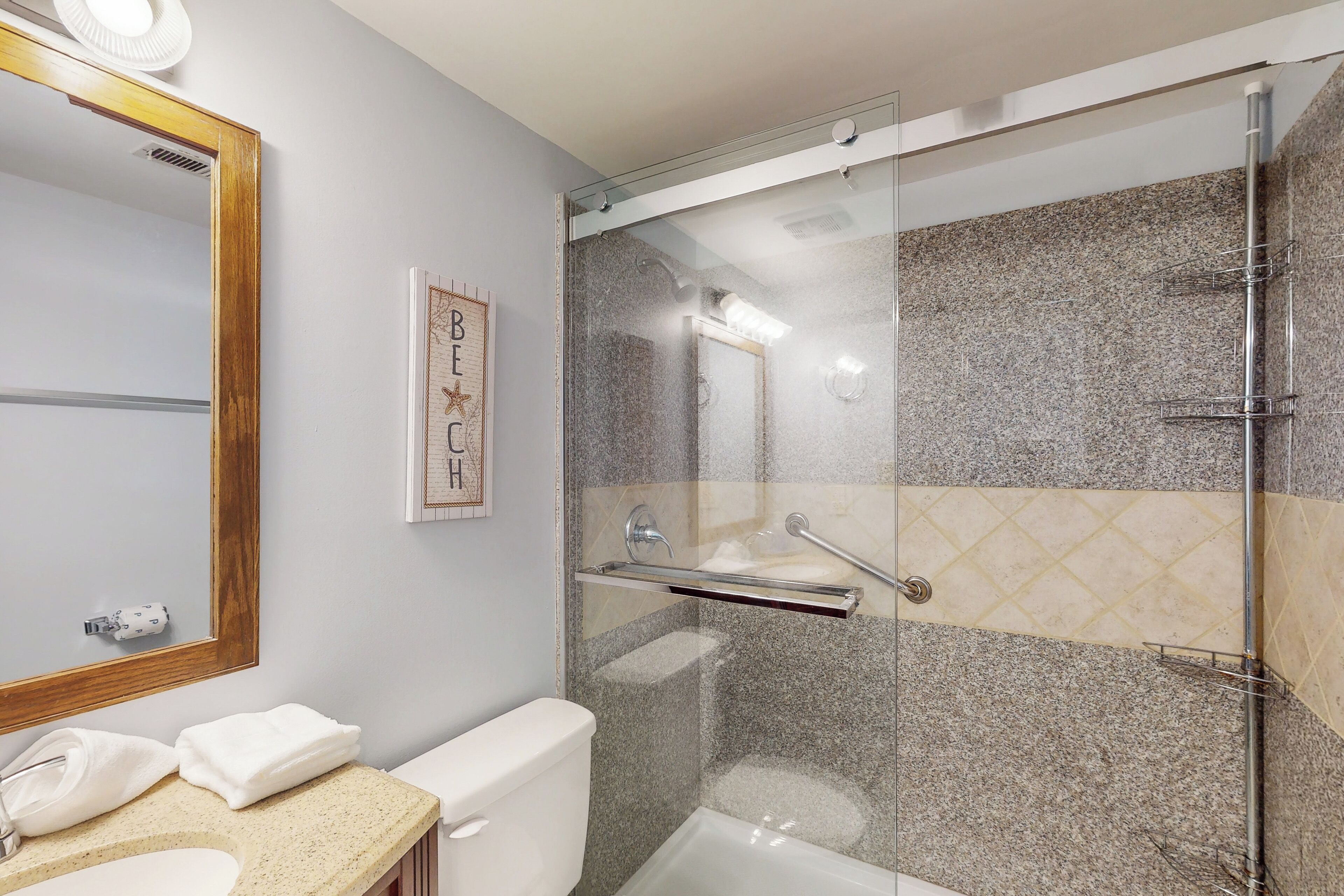 Une salle de bain moderne avec une douche à parois de verre, des toilettes blanches et un plan de toilette beige avec un lavabo.