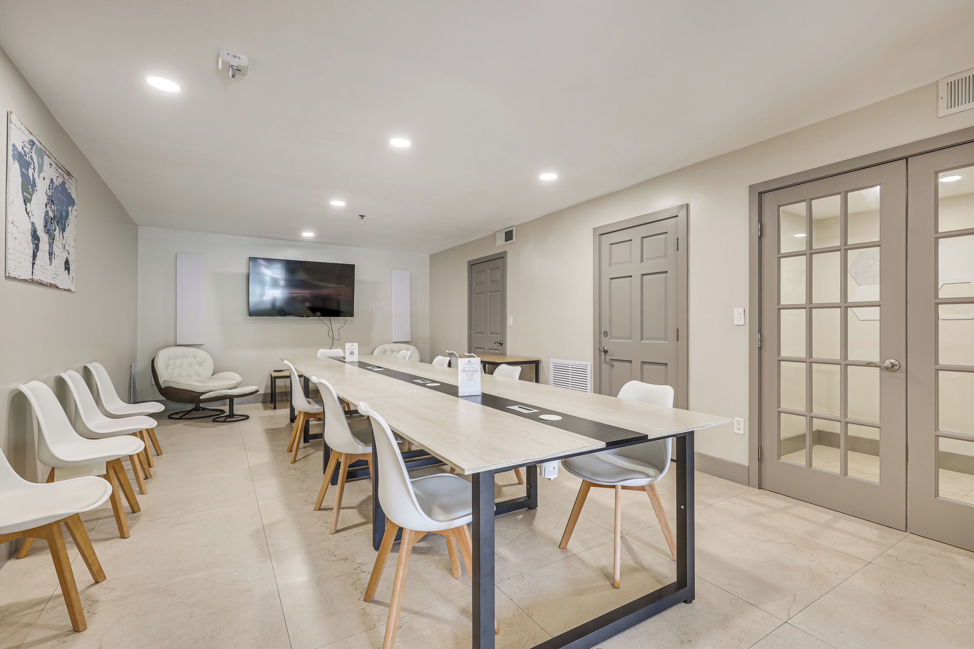 A conference room with a long table, several chairs, a television, and a world map on the wall.