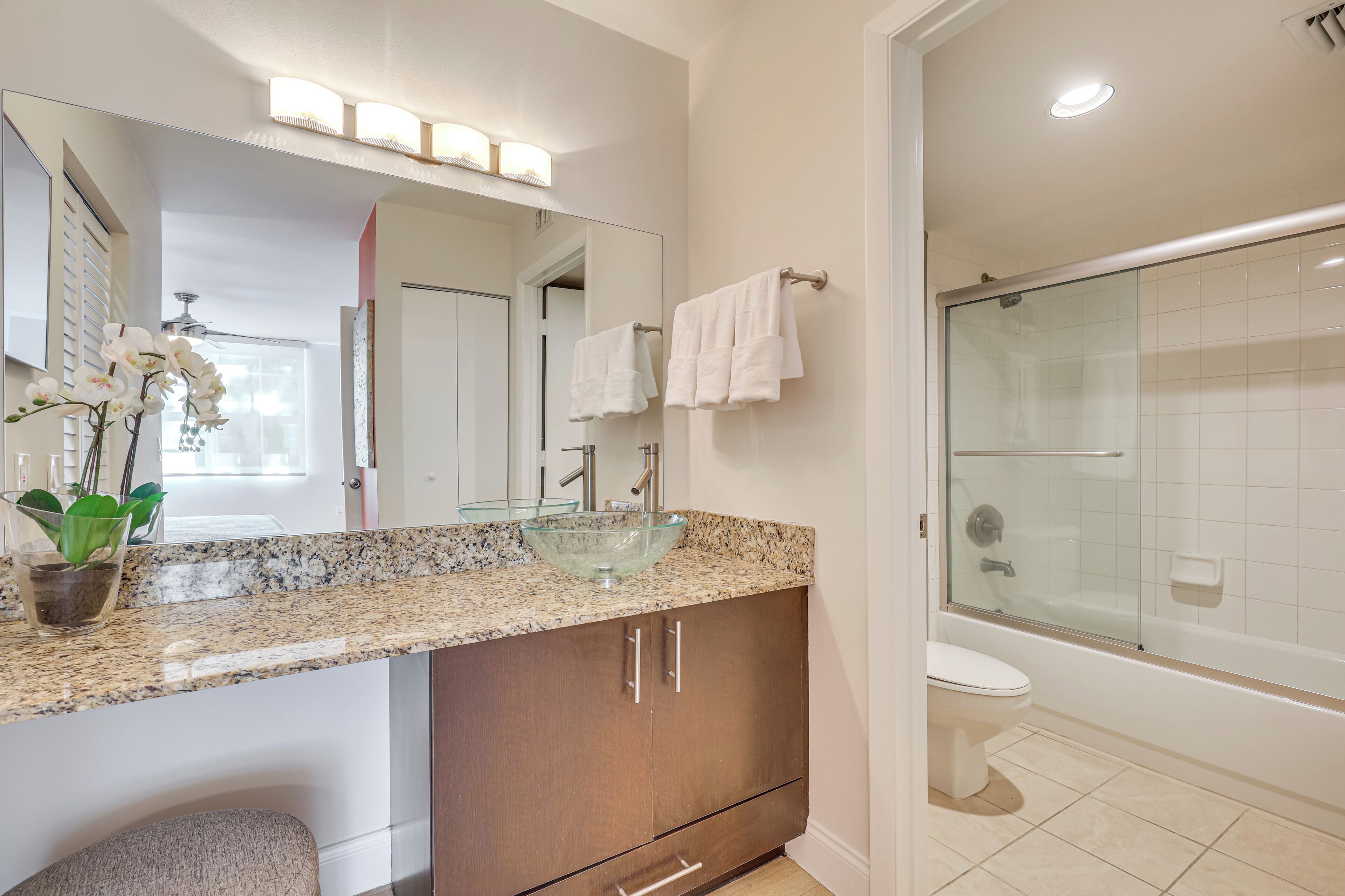 A modern bathroom with a glass sink, a large mirror, and a walk-in shower.