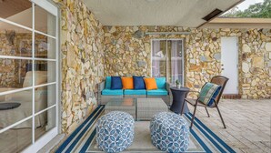 Une terrasse dallée de pierres, avec un canapé, des poufs et un fauteuil.