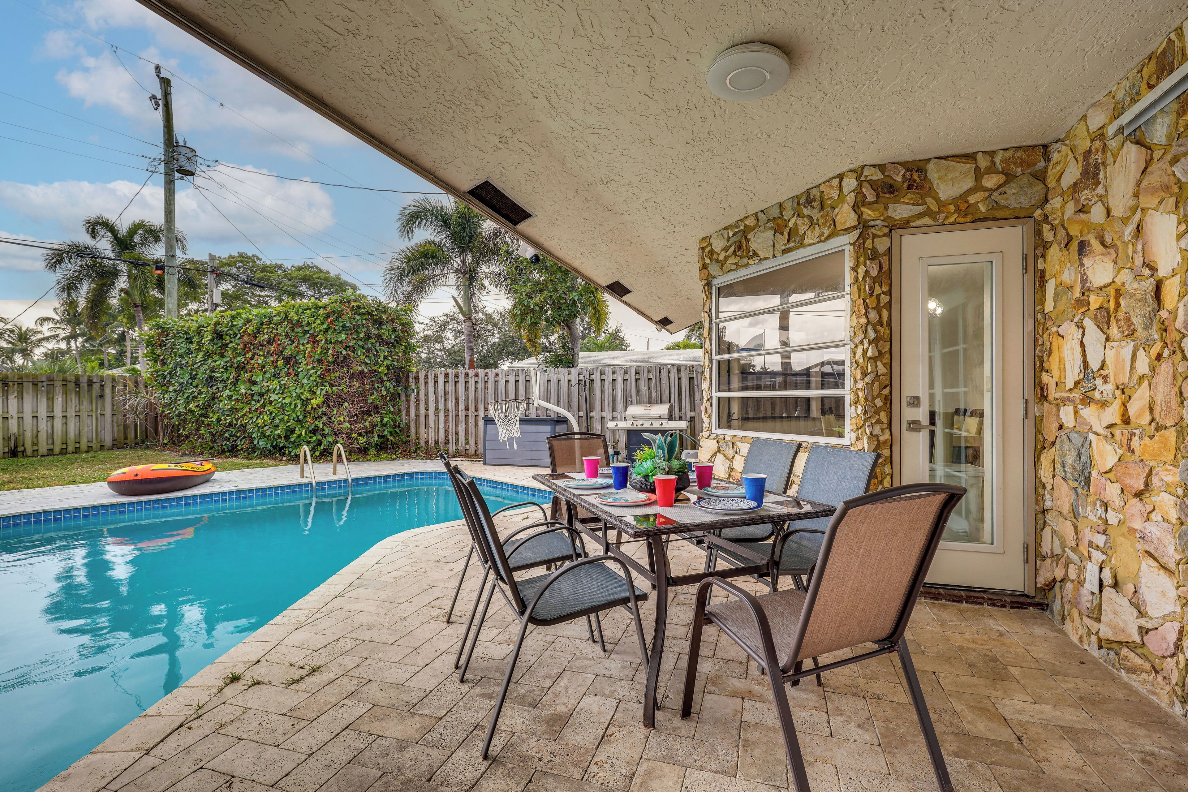 A patio with a pool, stone wall, and a table with chairs.