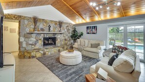 Un vaste espace de vie agrémenté d’une cheminée en pierre, d’un grand pouf rond et d’un mobilier confortable.