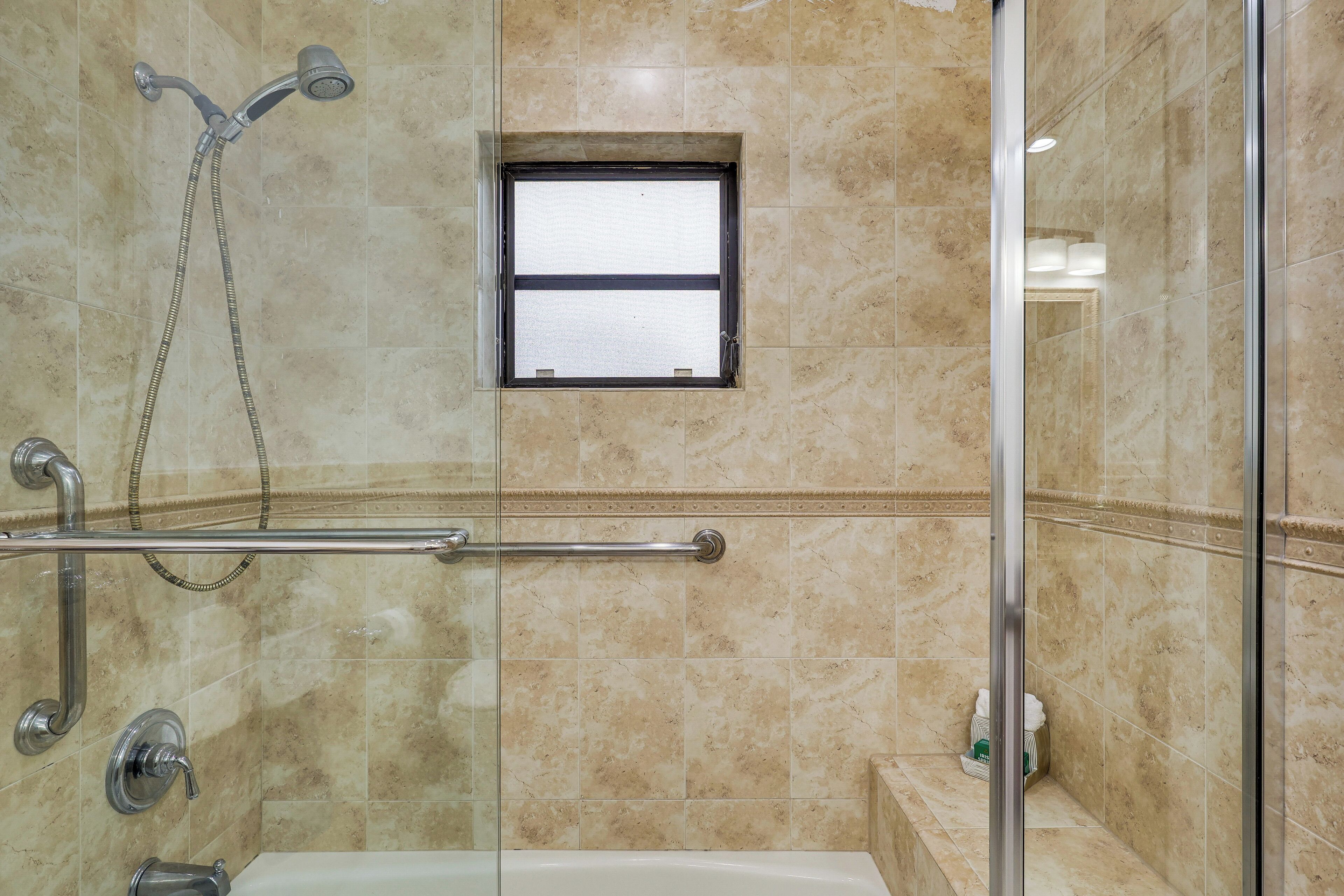 A bathroom with a glass-enclosed shower, a grab bar, and a small window.