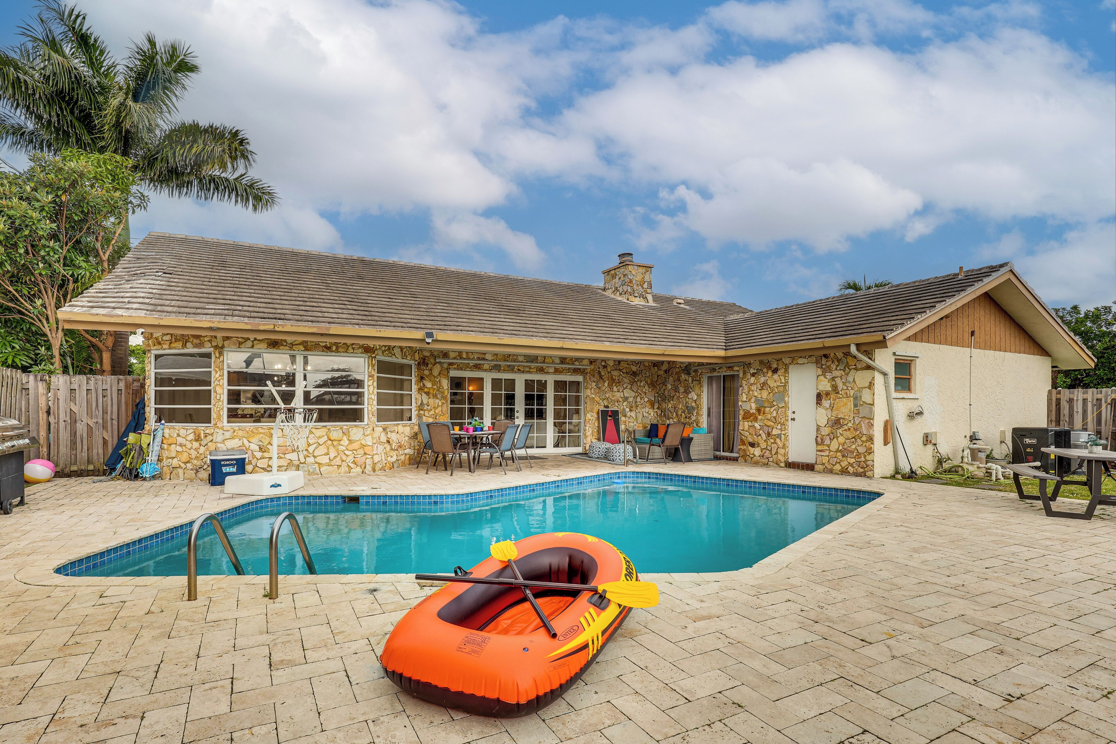 A house with a swimming pool, stone exterior, and a covered patio area.