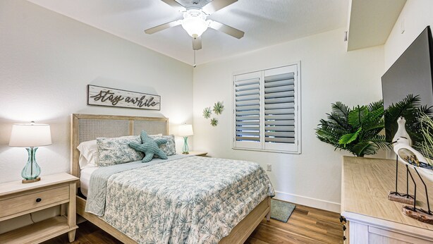 A bedroom with a bed, nightstands, a ceiling fan, a window with shutters, and a wall-mounted TV. - 8 Mi to Dtwn Naples: Condo w/ Resort Amenities! (Naples)