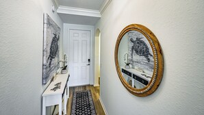 A hallway with a white door, a console table with decorative items, a patterned rug, and a wall-mounted mirror with a wooden frame. - 8 Mi to Dtwn Naples: Condo w/ Resort Amenities! (Naples)