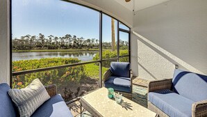 A sunlit room with a curved glass wall, wicker furniture, and a view of a lake and trees. - 8 Mi to Dtwn Naples: Condo w/ Resort Amenities! (Naples)