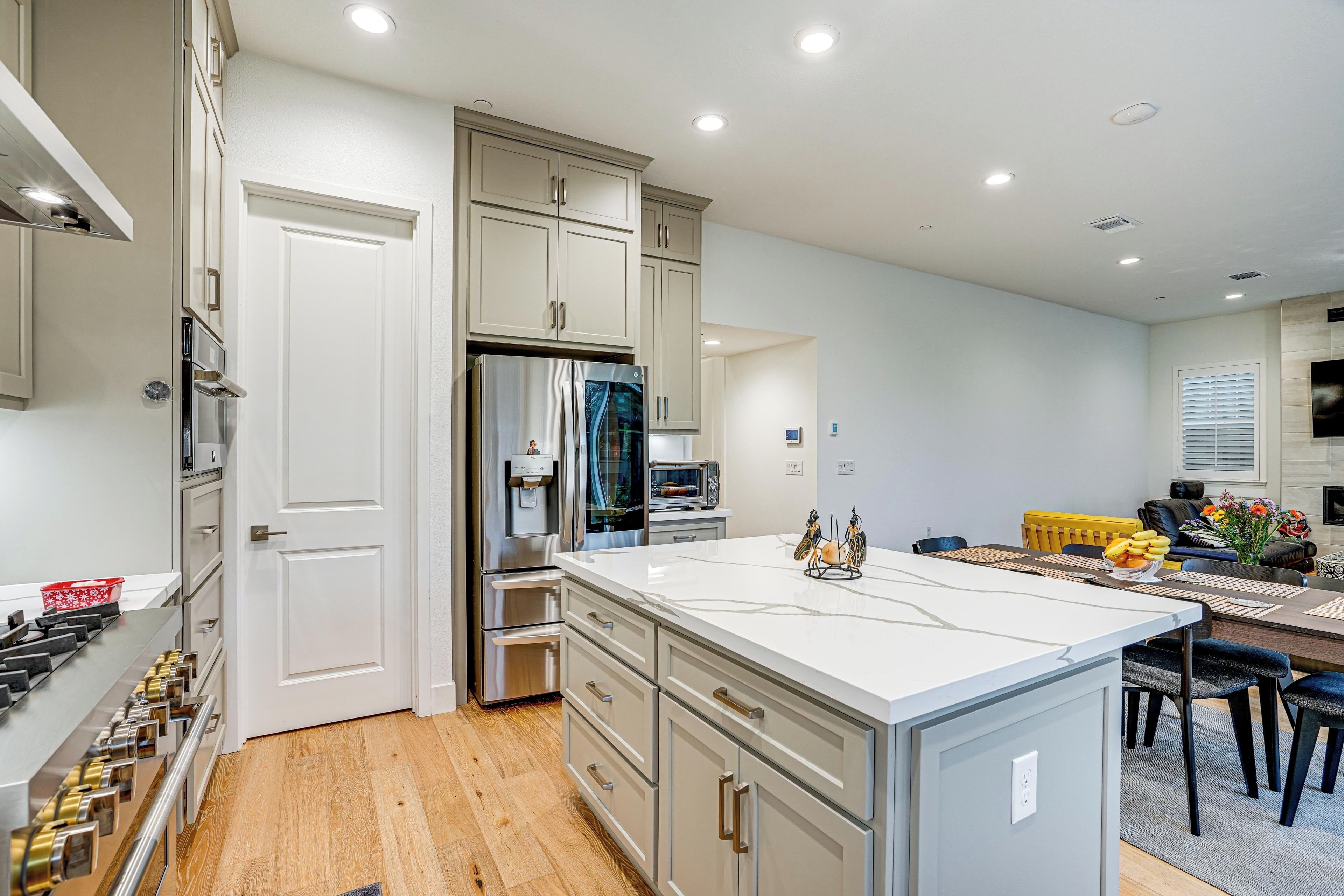 A modern kitchen with stainless steel appliances, a large island, and a dining area with a yellow chair.