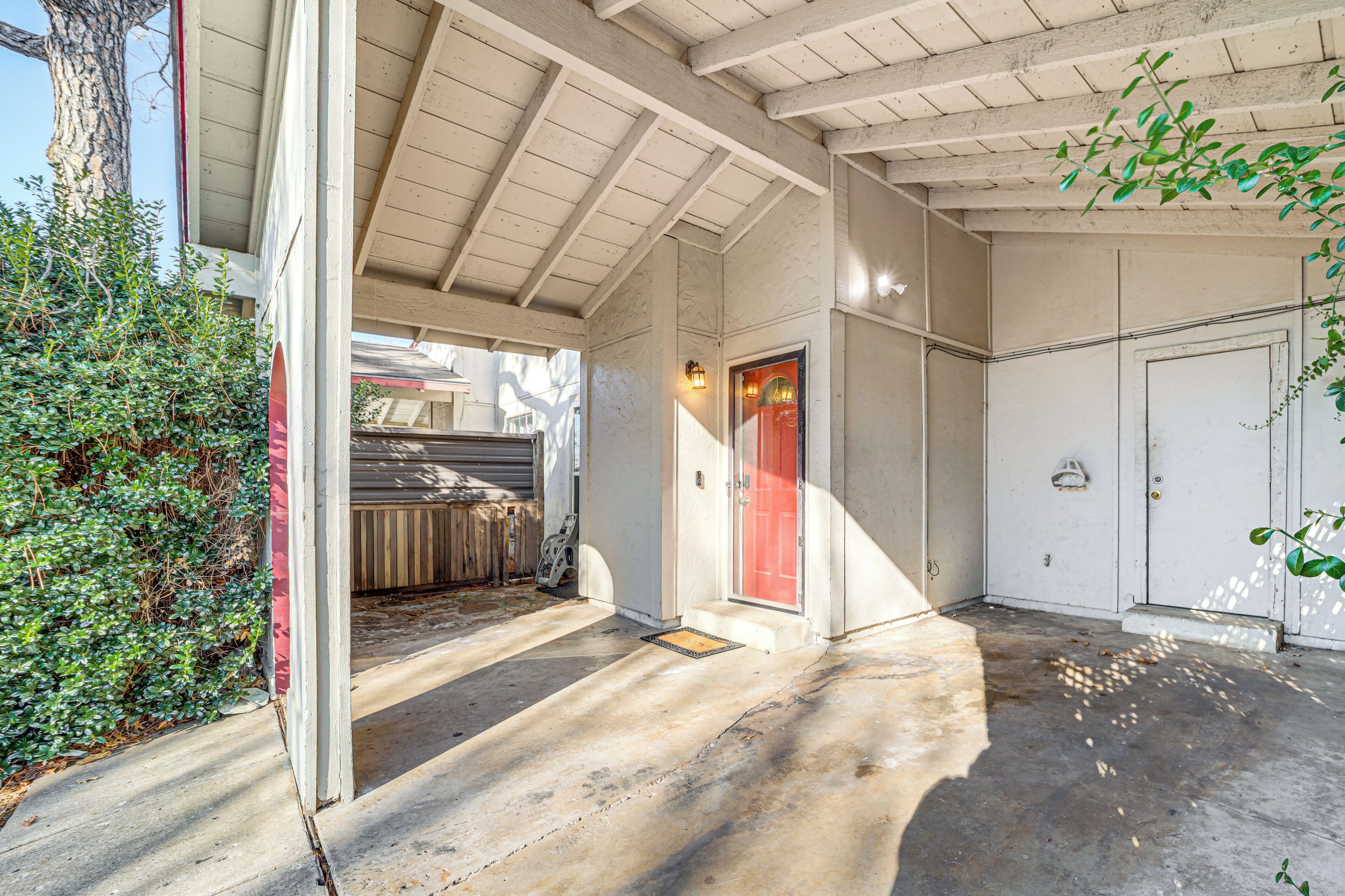 A covered outdoor area with a red door, a concrete floor, and a wooden ceiling.