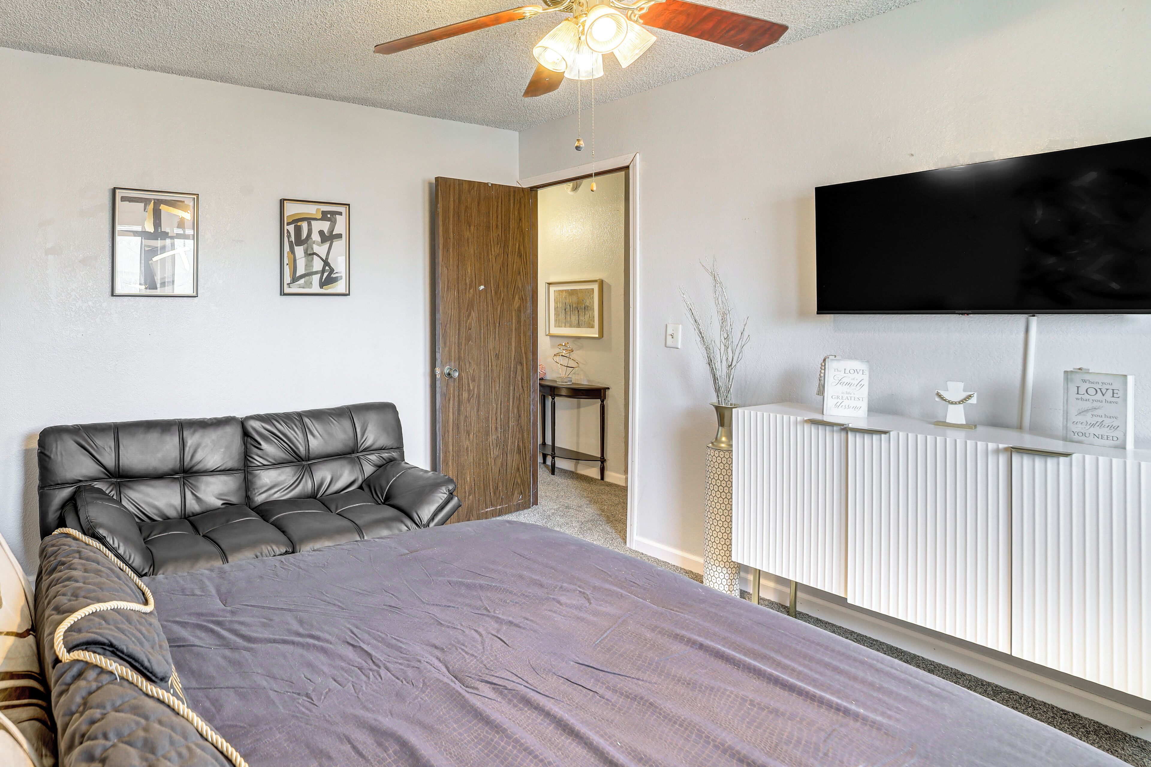 A bedroom with a large bed, a ceiling fan, a mounted TV, and a bedside table with decorative items.