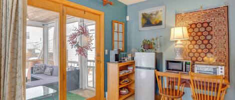 A compact kitchen with a refrigerator, microwave, toaster, and wooden chairs.