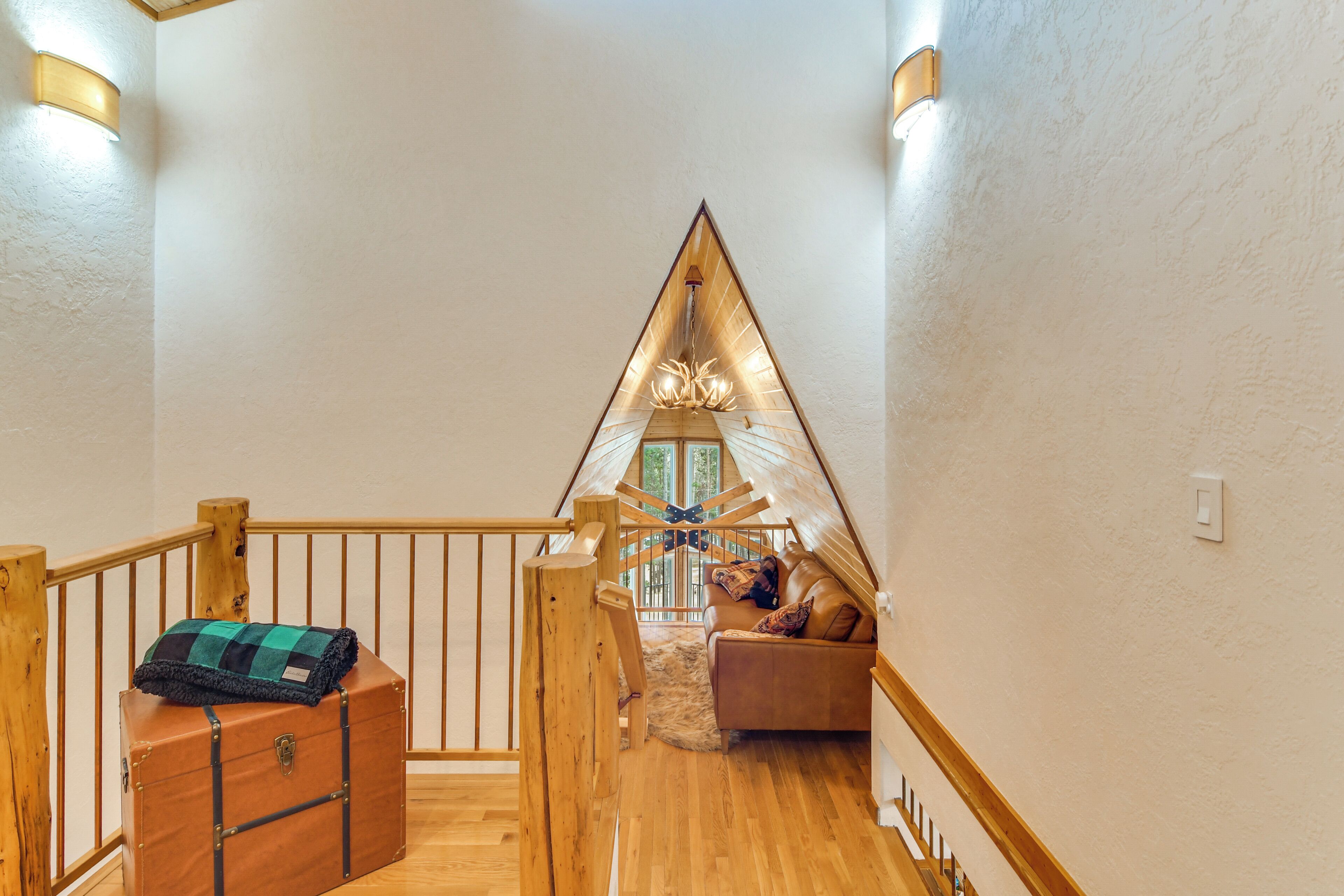 A loft bedroom with a sloped ceiling, wooden staircase, and a cozy seating area with a sofa and a decorative chandelier.