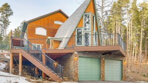 A log cabin with a balcony, a garage, and a staircase leading to the main entrance. - Wooded Retreat w/ Private Hot Tub in Evergreen (Evergreen)