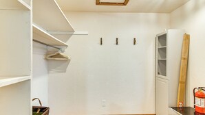 A room with a wooden floor, white walls, a white wardrobe, a hanging garment, and a fire extinguisher. - Wooded Retreat w/ Private Hot Tub in Evergreen (Evergreen)