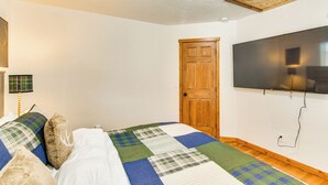 A bedroom with a bed, a wooden door, a television mounted on the wall, and a ceiling light fixture. - Wooded Retreat w/ Private Hot Tub in Evergreen (Evergreen)