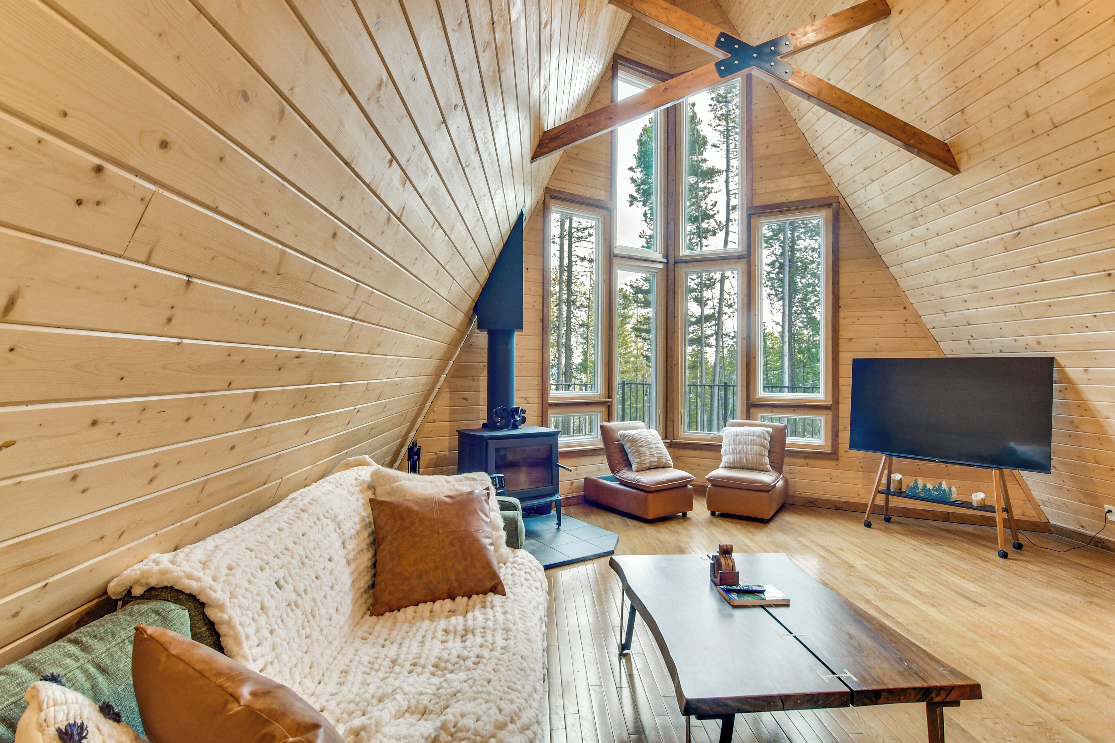L’intérieur d’un chalet en bois chaleureux et accueillant, avec un canapé, des fauteuils, un téléviseur et une cheminée.