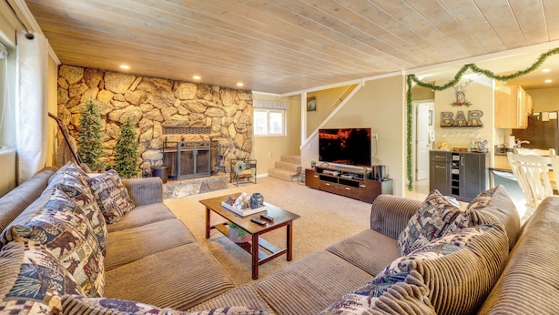 A cozy living room with a stone fireplace, a large sofa set, and a television. - Hot Tub + Game Room: Group Getaway in Big Bear! (Sugarloaf)