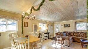 A cozy living room with a wooden ceiling, a dining area with a wooden table and chairs, and a patterned sofa. - Hot Tub + Game Room: Group Getaway in Big Bear! (Sugarloaf)