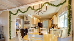 A dining area with a wooden table and white chairs, surrounded by kitchen cabinets and a chandelier. - Hot Tub + Game Room: Group Getaway in Big Bear! (Sugarloaf)