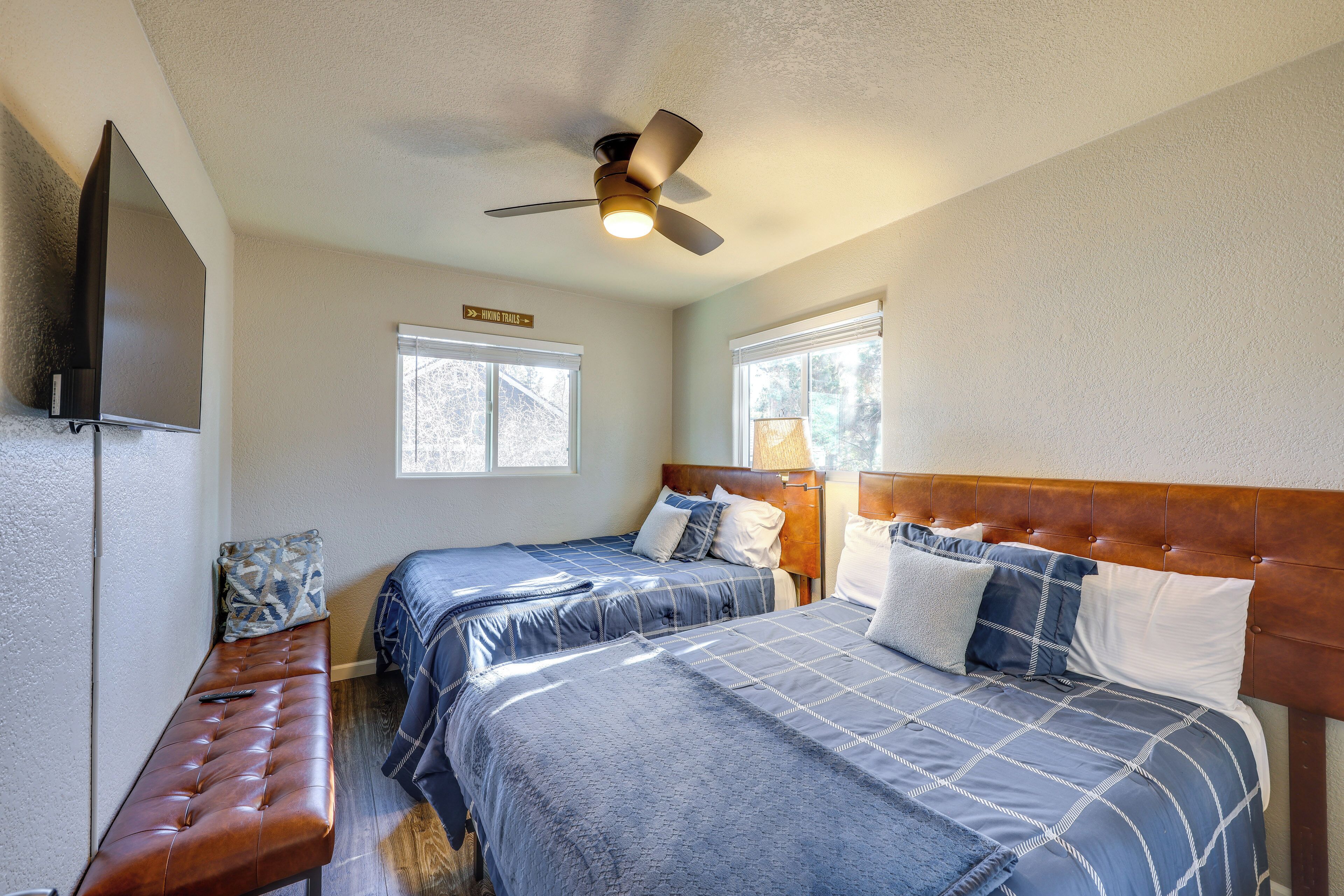 A bedroom with two beds, a bench, a ceiling fan, and a TV.