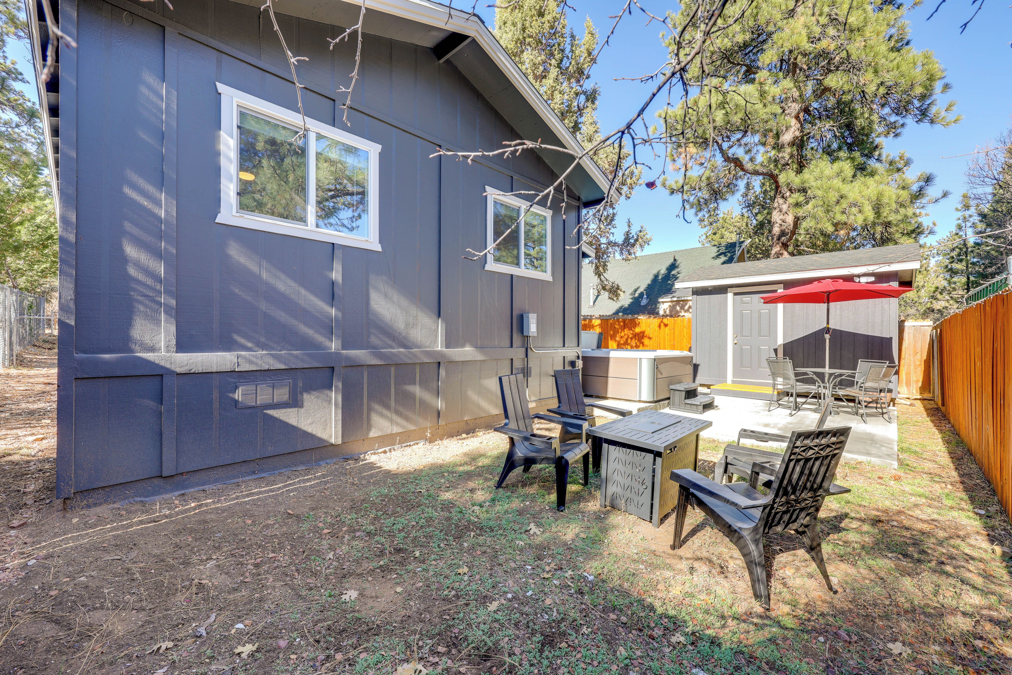 A backyard with a patio area, including a table and chairs, a wooden bench, and a red umbrella.